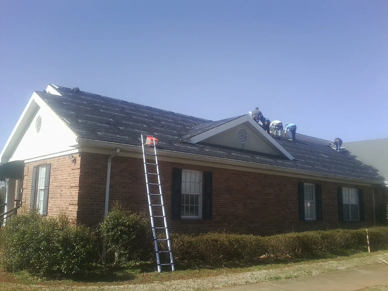 Crew tearing shingles off a brick ranch roof with a ladder set — Metal Roof Repair work by our crew in Evergreen