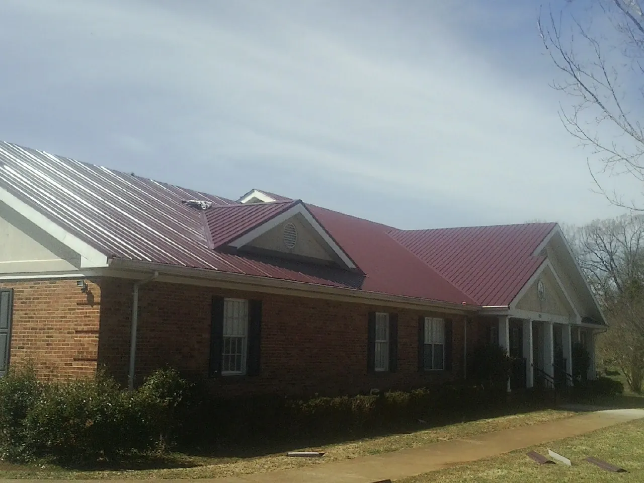 Red metal roof with gabled entries on a long brick building, from a Hail Damage Roof Repair job in Evergreen