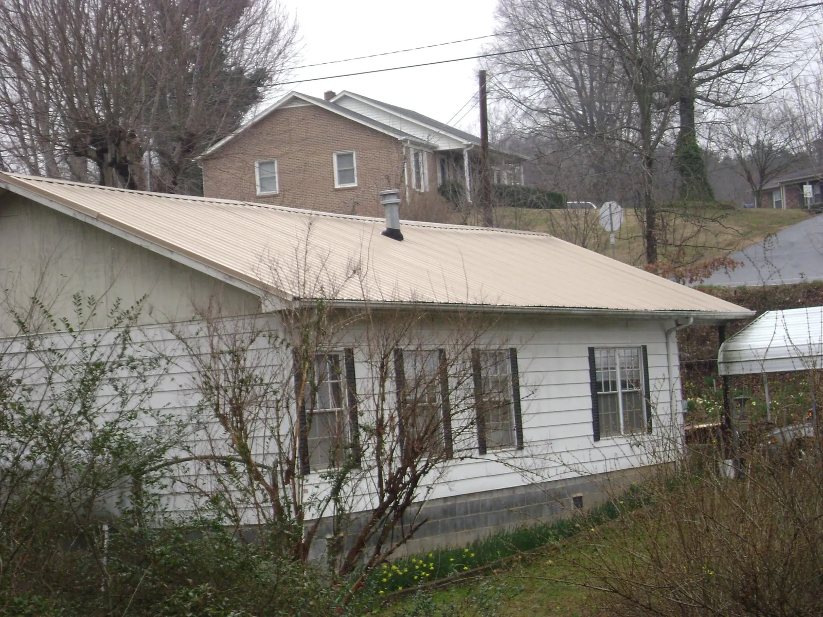Tan metal roof on a white sided house set into a hillside — Commercial Roofing by Roofing Brothers in Evergreen